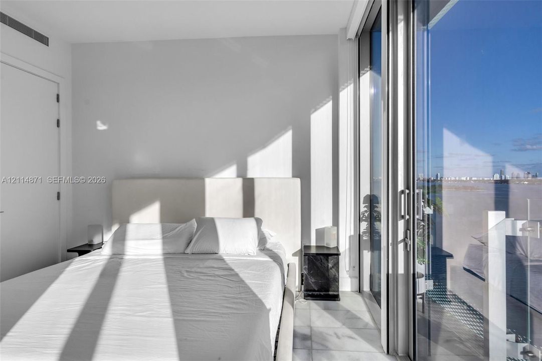 Floor-to-ceiling glass sliding doors, stone tile flooring, and a private balcony featuring a glass panel railing