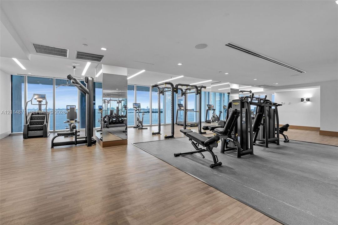 Fitness center featuring floor-to-ceiling windows, wood-finish flooring, recessed lighting, and mirrored support columns
