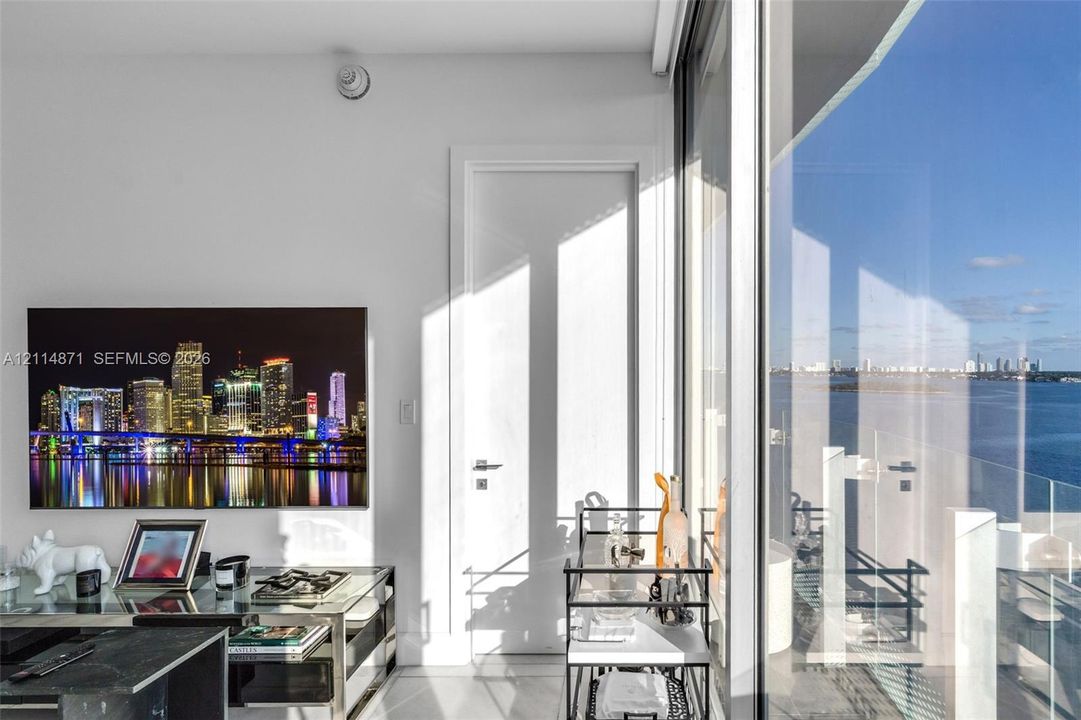 Floor-to-ceiling glass sliding doors, private glass-railing balcony, and expansive water and urban skyline scenery