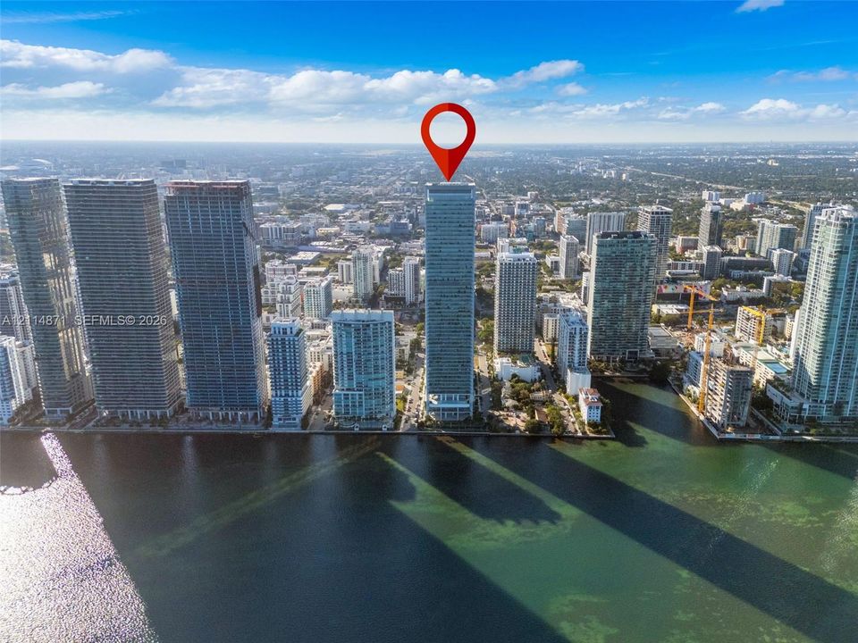 Aerial perspective of a high-rise tower featuring a glass facade, expansive water frontage, and urban skyline positioning