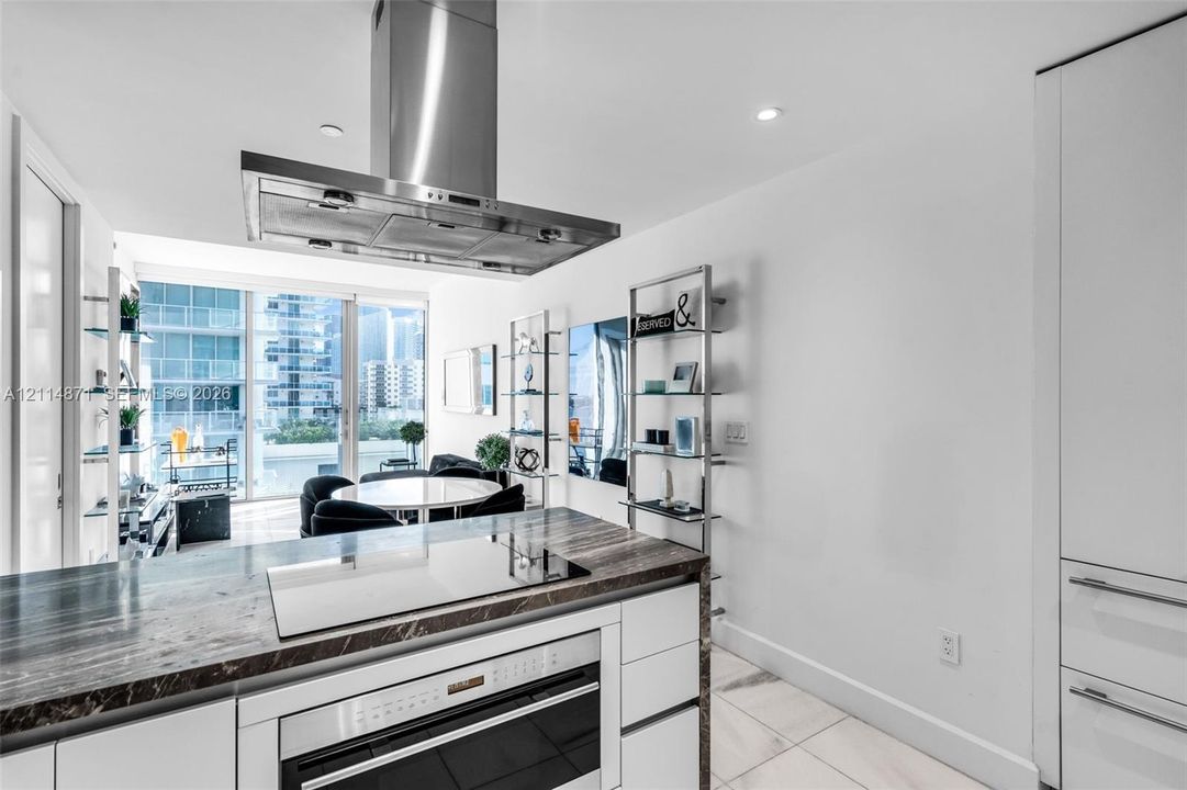 Kitchen featuring an island with stone-finish countertop, built-in cooktop, stainless steel vent hood, floor-to-ceiling cabinetry, and light-tone tile flooring