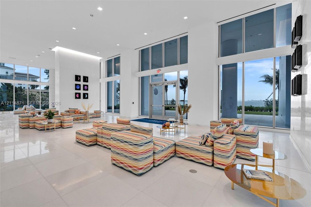 Expansive lobby featuring floor-to-ceiling glass walls, polished stone flooring, recessed ceiling lighting, and double-entry glass doors