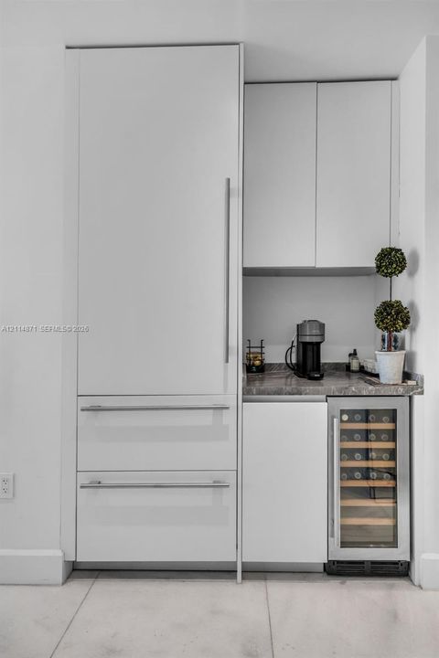 Built-in refrigerator with panel-ready cabinetry, stone countertop, upper and lower cabinetry, and under-counter wine storage