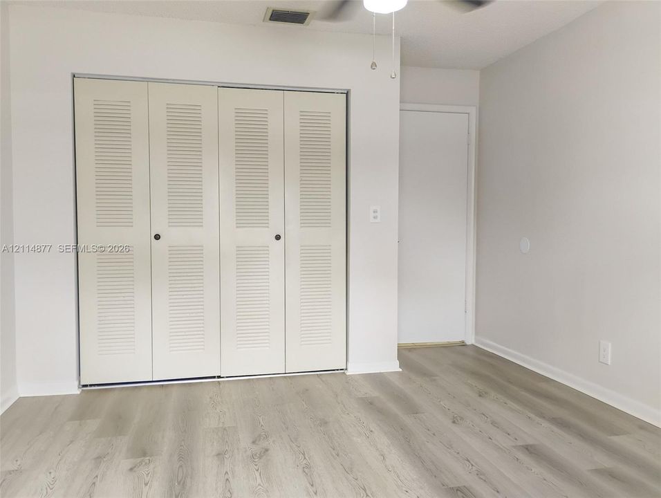 Wood-finish flooring, white walls, four-panel louvered closet doors, and a ceiling-mounted light fixture