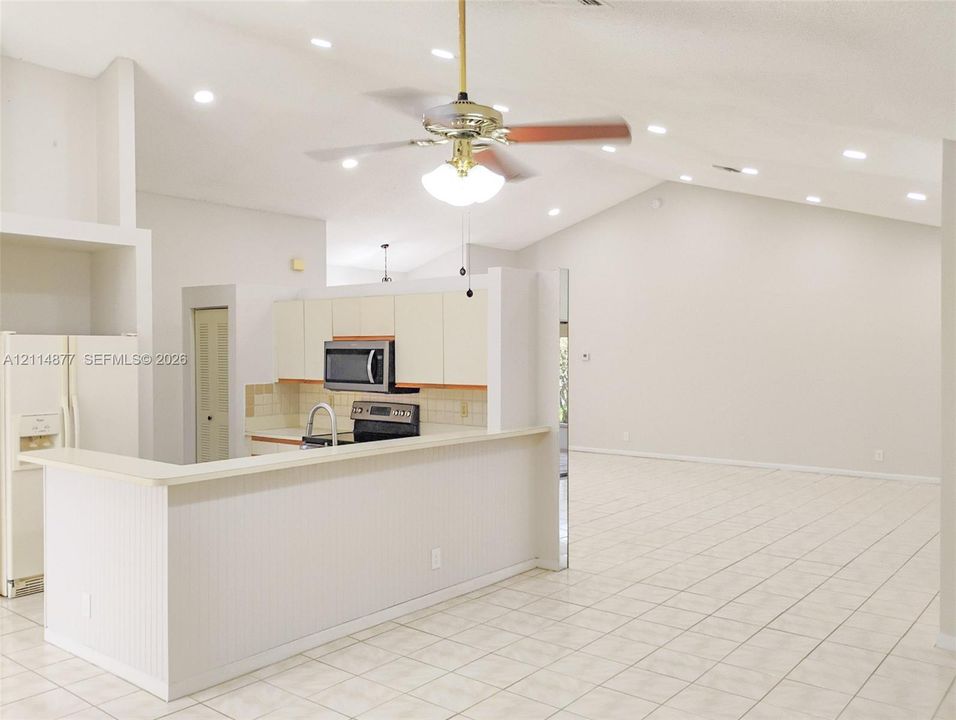 Vaulted ceilings featuring recessed lighting, a pass-through kitchen peninsula, tile flooring, and a ceiling fan with integrated lighting