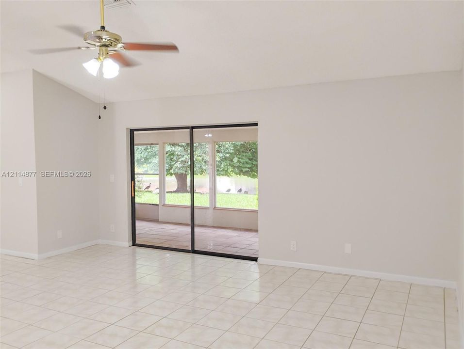 Living area featuring tile flooring, vaulted ceilings, a central ceiling fan with multi-light fixture, and sliding glass doors with exterior screen enclosure