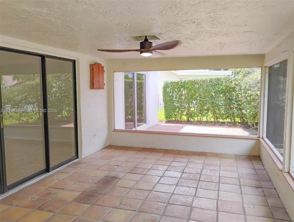 Covered patio featuring ceramic tile flooring, sliding glass doors, ceiling fan, and large picture windows