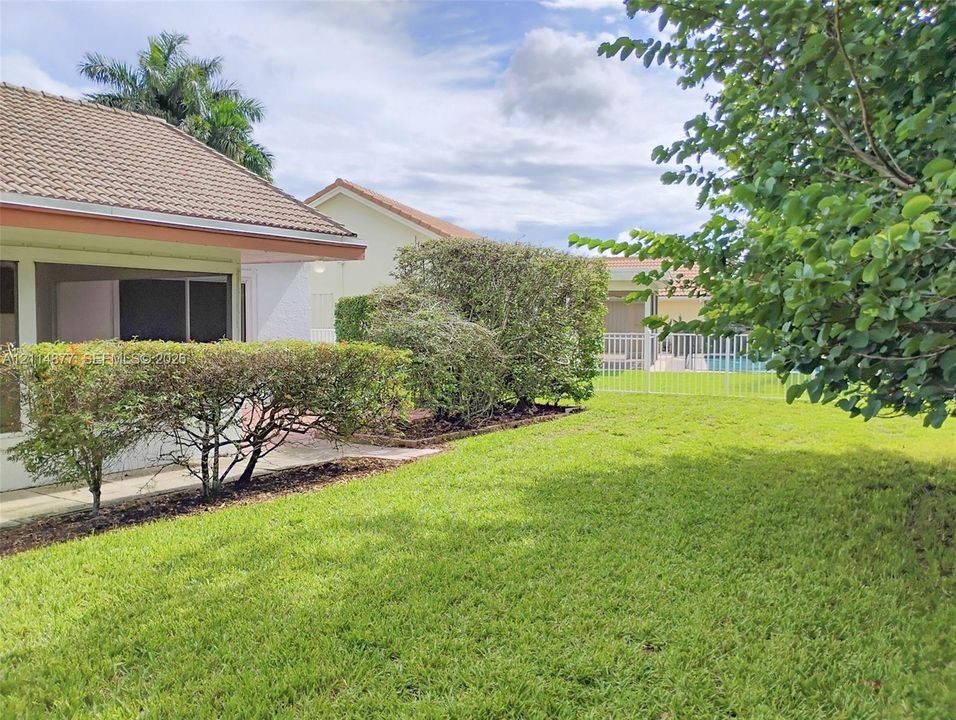 Private backyard featuring a manicured lawn, established shrubbery, mature trees, and a fenced swimming pool area