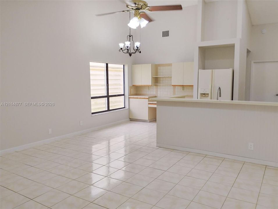 Vaulted ceilings featuring a chandelier and ceiling fan, tile flooring, and kitchen cabinetry with integrated counter space