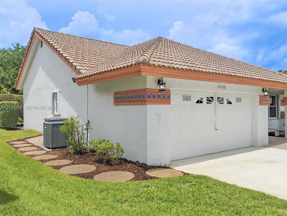 Stucco exterior featuring a tiled roof, decorative patterned trim, two-car garage with overhead door, and concrete driveway