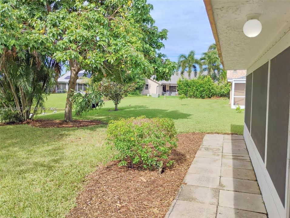 Expansive backyard featuring a manicured lawn, mature trees, mulched landscaping, and a concrete paver walkway