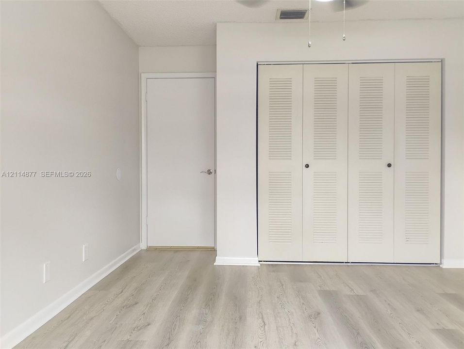 Wood-finish flooring, neutral wall tones, closet with bi-fold louvered doors, and ceiling-mounted light fixture