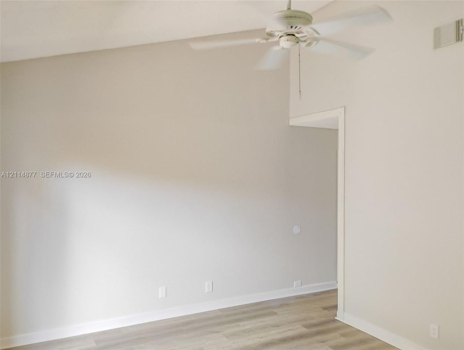 Vaulted ceiling featuring a central white ceiling fan and light fixture, complemented by light-toned wood-finish flooring