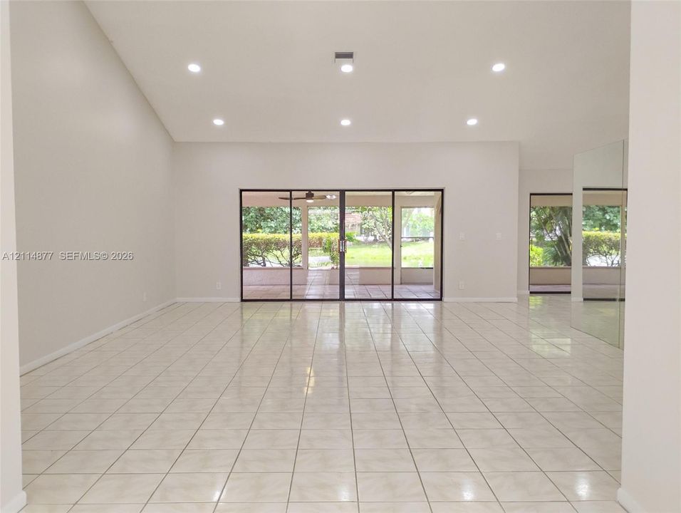 Vaulted ceilings, neutral tile flooring, recessed lighting, and large sliding glass doors
