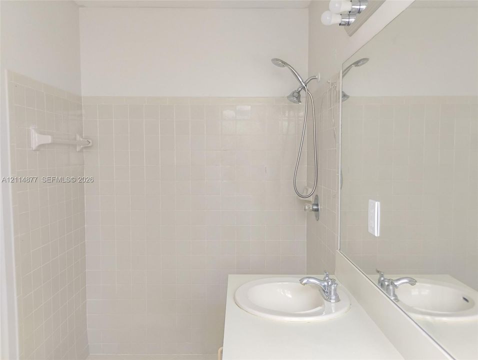 Full-height tile shower enclosure featuring a handheld showerhead, integrated vanity with a circular drop-in sink, and a large-format vanity mirror with overhead light fixture