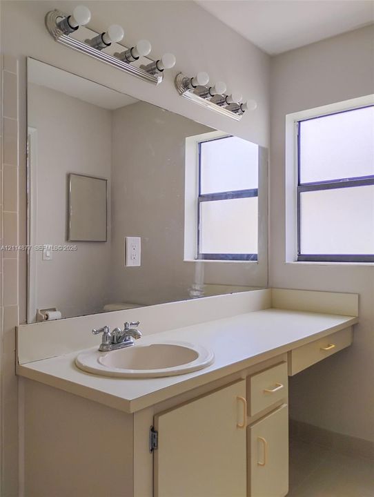 Vanity featuring a solid-surface countertop with an integrated basin, chrome-finish faucet, multi-drawer cabinetry, and a large wall-mounted mirror with an overhead multi-bulb light fixture