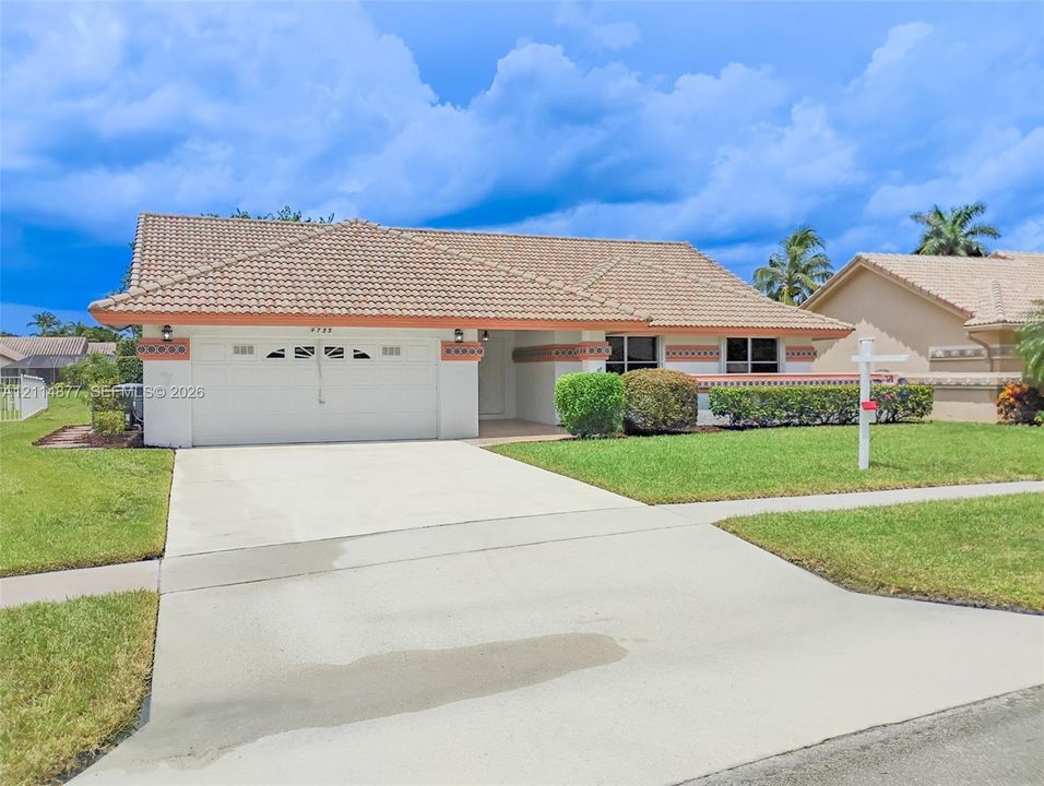 Single-story exterior featuring a concrete tile roof, stucco facade, two-car garage with arched windows, and decorative trim details