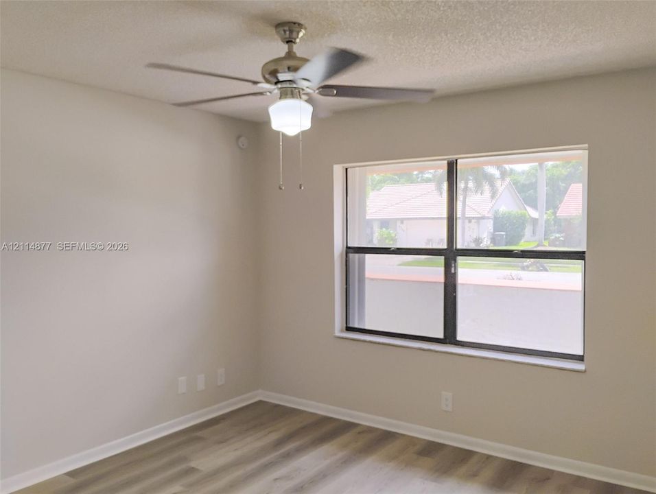Room featuring wood-finish flooring, a neutral wall palette, a large rectangular window with a dark frame, and a polished nickel ceiling fan with an integrated light fixture