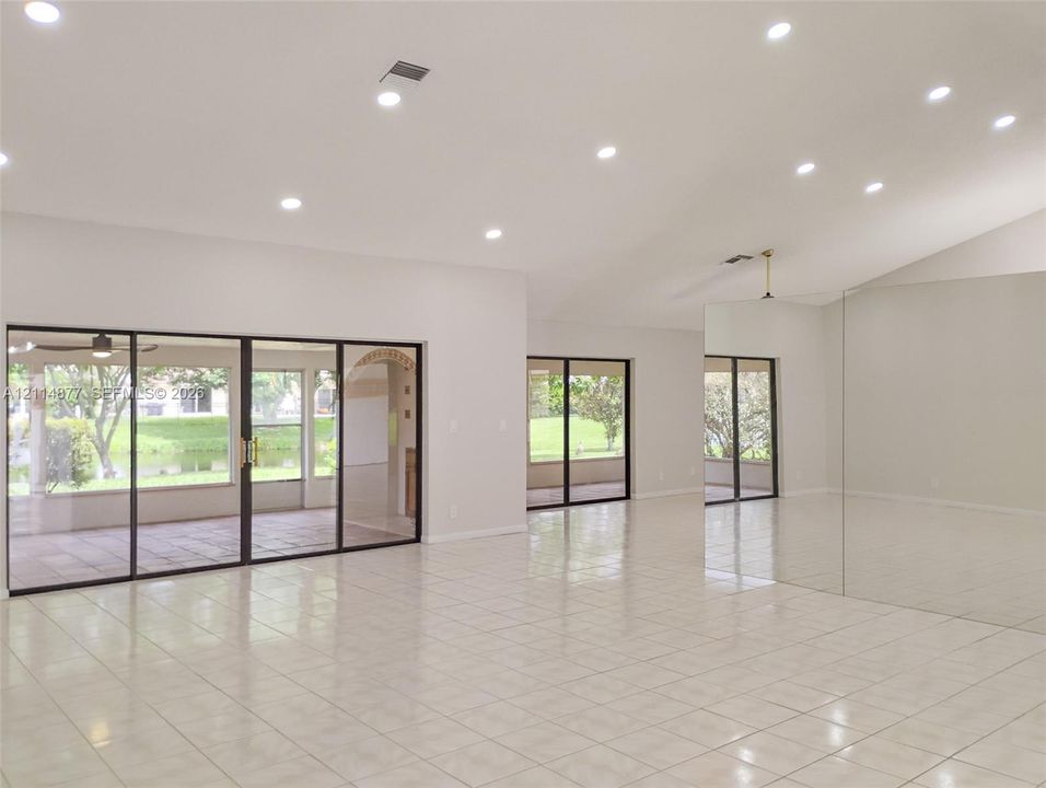 Open living space featuring vaulted ceilings, recessed lighting, tile flooring, mirrored wall panels, and multiple sliding glass door sets