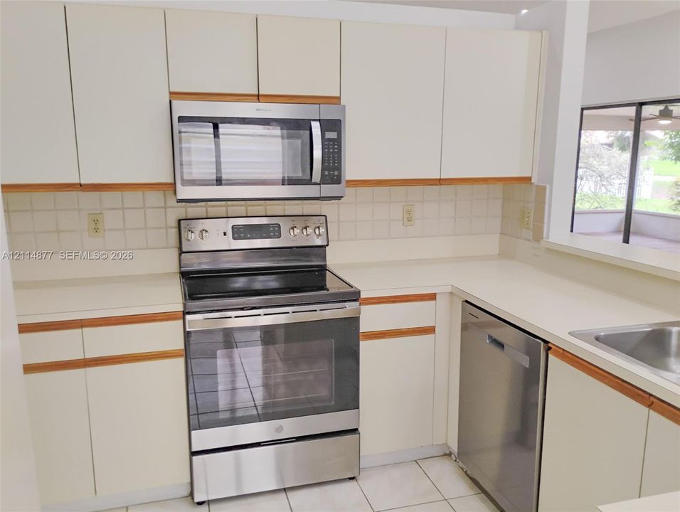 Kitchen featuring white cabinetry with wood trim, stainless steel appliances, solid surface countertops, a tiled backsplash, and tile flooring