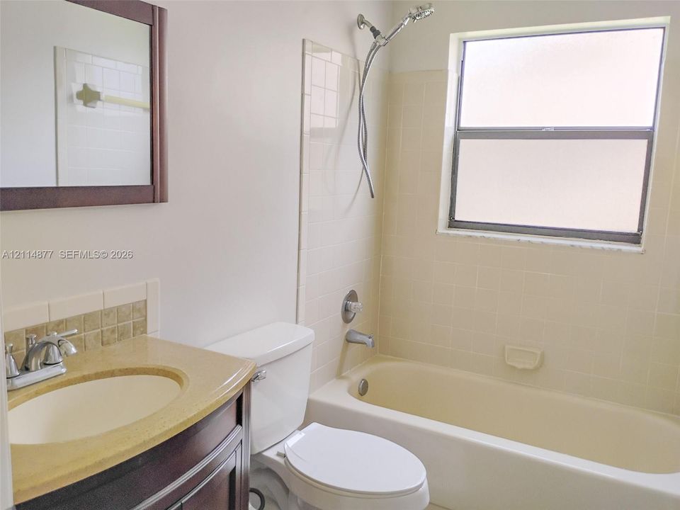 Bathroom featuring a dark wood-finish vanity with a light-toned solid surface countertop, an integrated sink, a tiled shower surround, and a window