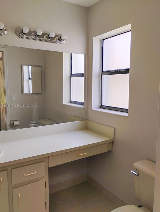 Built-in vanity with integrated countertop, large wall-mounted mirror, polished chrome four-light fixture, and privacy glass window