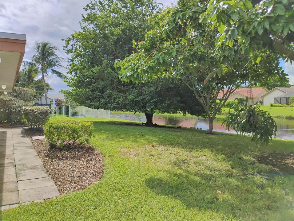 Expansive backyard featuring a concrete paver patio, manicured lawn, mature trees, and direct water frontage