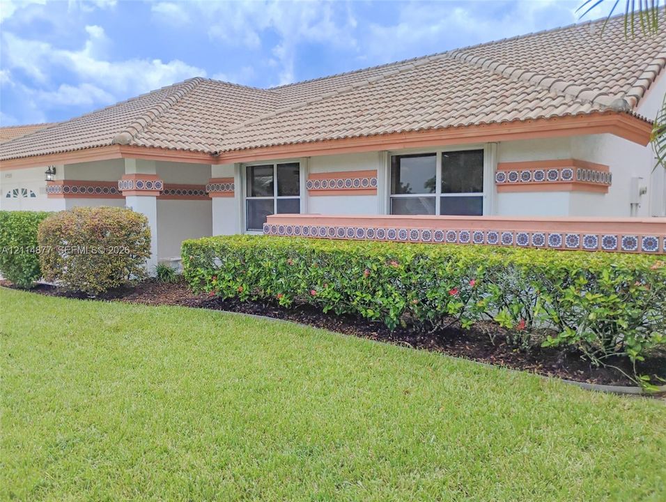 Single-story exterior featuring a concrete tile roof, stucco finish, custom decorative tile banding, and integrated hardscaping