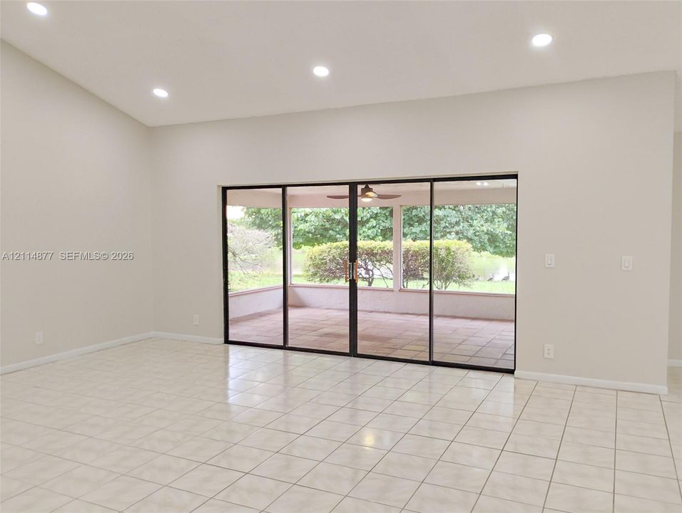 Vaulted ceilings with recessed lighting, large-format tile flooring, and oversized sliding glass doors opening to a covered paved patio