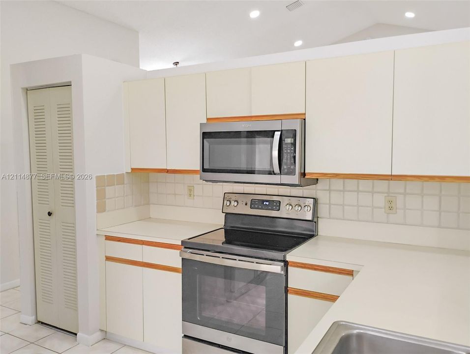 Kitchen featuring off-white cabinetry with wood-tone accents, integrated stainless steel microwave, stainless steel electric range, tile backsplash, and solid-surface countertops