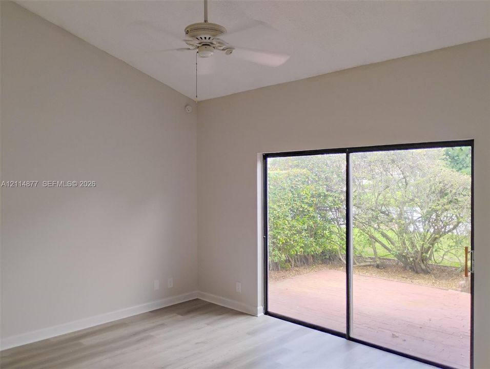 Vaulted ceilings, wood-finish flooring, ceiling fan, and sliding glass doors opening to a brick patio