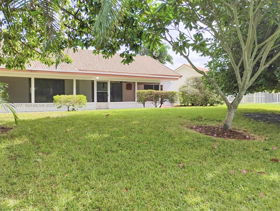 Spacious rear lawn featuring mature landscaping, a tiled roofline, and a covered patio area with screen enclosure