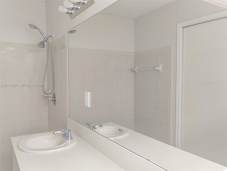 Bathroom featuring an integrated vanity with a molded basin, a wall-to-wall mirror, ceramic wall tiling, a handheld shower fixture, and an attached towel bar