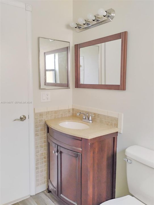 Dark-finish wood vanity featuring a neutral-toned stone countertop, integrated sink with chrome faucet, square-tiled backsplash, and coordinating framed vanity mirror