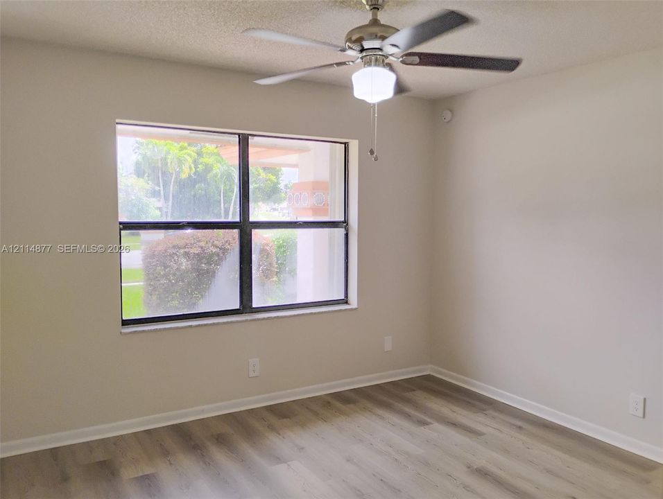 Room featuring wood-finish flooring, a neutral color palette, a large horizontal window, and a multi-blade ceiling fan with an integrated light fixture