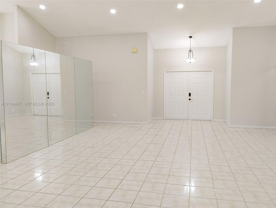 Vaulted ceilings, large-format tile flooring, double-entry doors with multi-panel detail, full-wall mirrored paneling, and recessed lighting