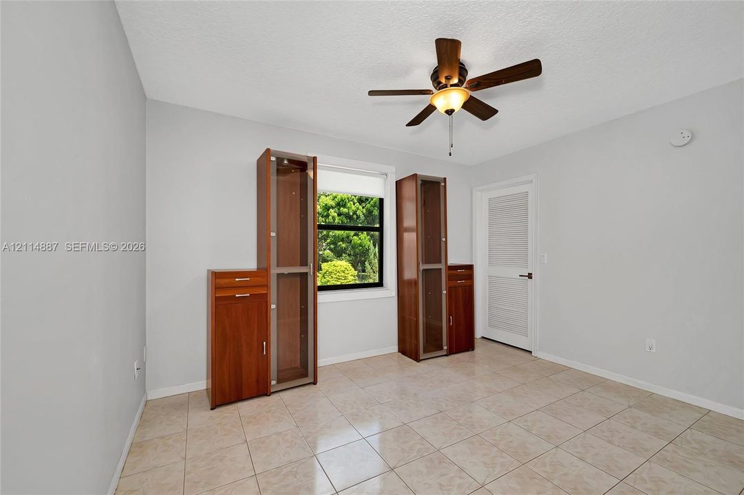 Room featuring neutral wall paint, tile flooring, built-in wooden cabinetry, a ceiling fan with integrated lighting, and a single-panel interior door