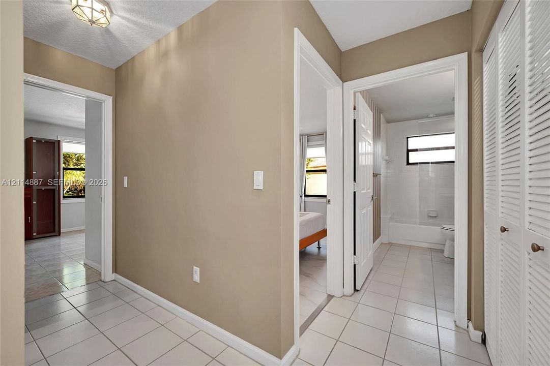 Neutral-toned hallway featuring ceramic tile flooring, recessed geometric lighting fixture, and floor-to-ceiling louvered closet doors