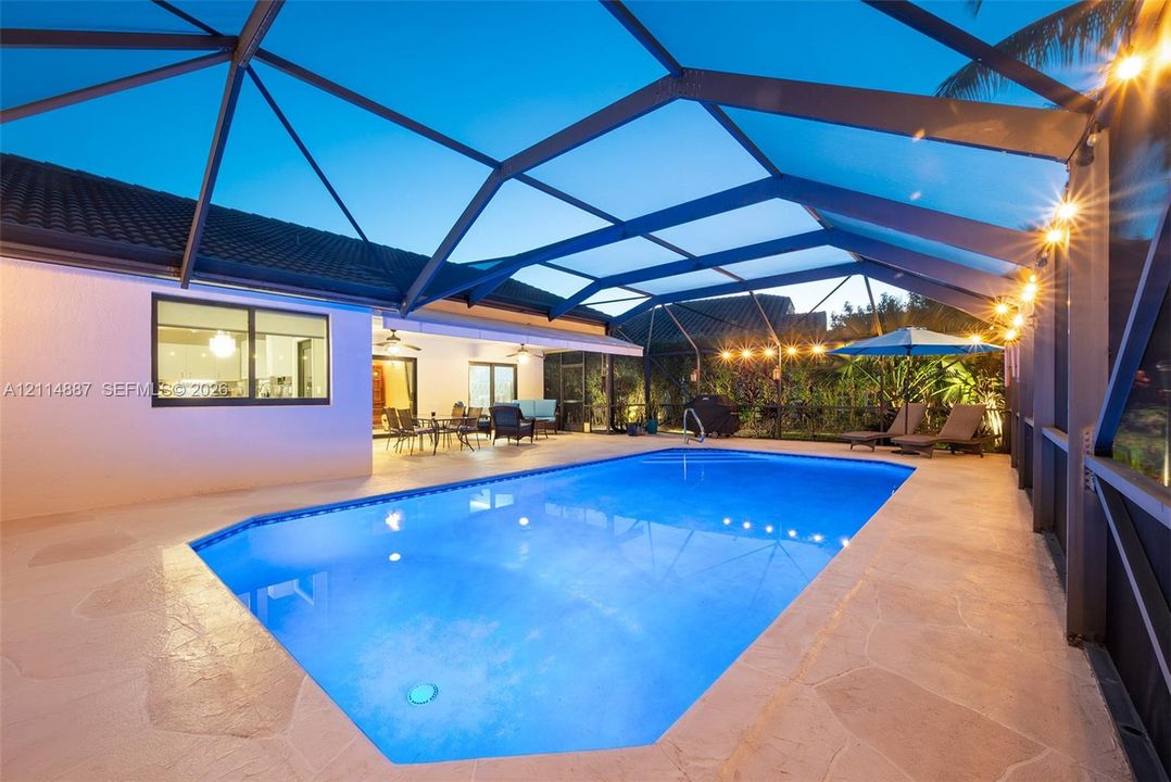Screened-in pool enclosure featuring a multi-faceted pool design, paver patio flooring, and covered lanai area