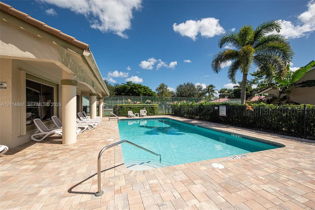 Outdoor swimming pool featuring a brick paver deck, covered patio with structural columns, and perimeter metal fencing