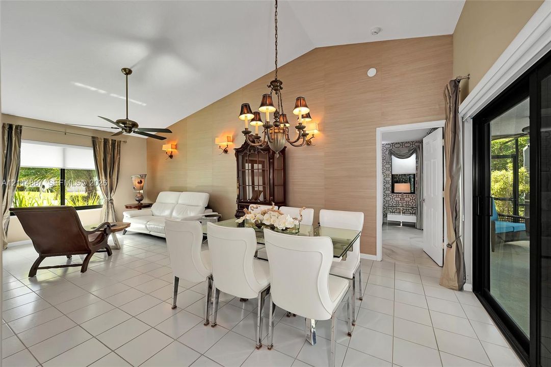 Vaulted ceilings, feature wall with textured surfacing, multi-arm chandelier, ceiling fan, and sliding glass doors with exterior access