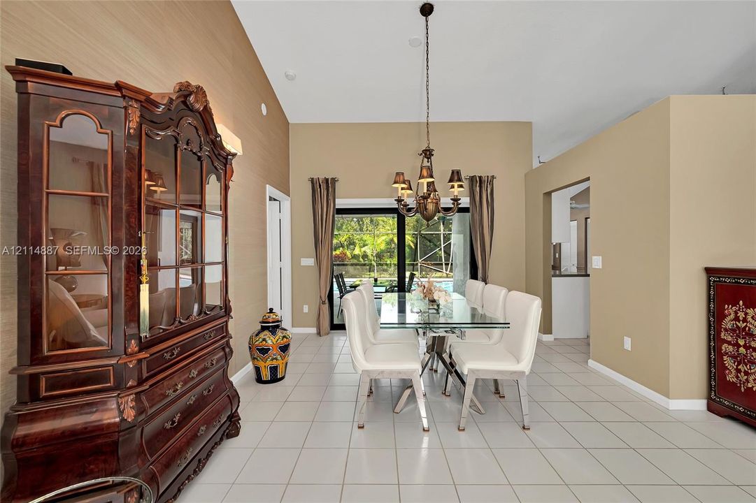 Vaulted ceilings, ceramic tile flooring, textured wall finishes, and a multi-arm metal chandelier, featuring sliding glass doors to a screened outdoor area