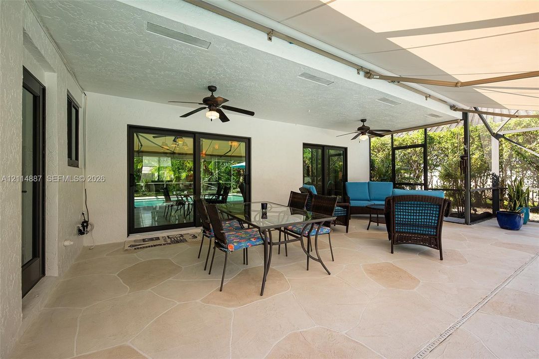 Covered patio featuring flagstone-style flooring, two ceiling fans, retractable awning, and screen enclosure