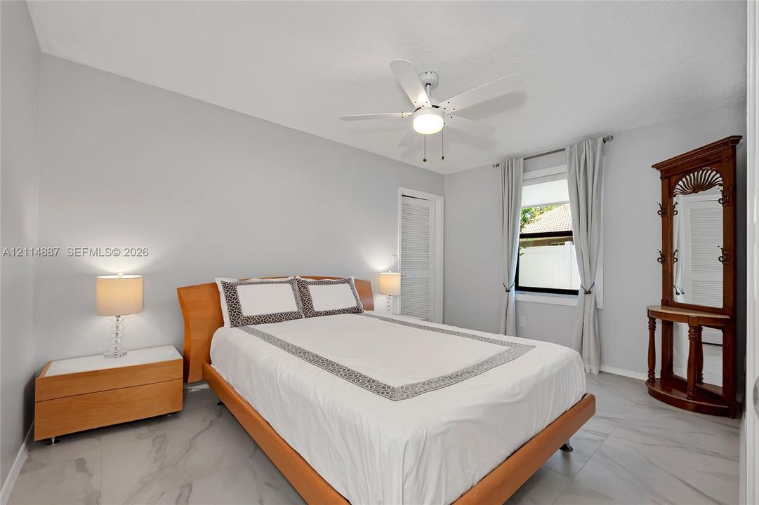 Neutral-toned room featuring large-format tile flooring, a white ceiling fan with integrated lighting, and a window with neutral drapery