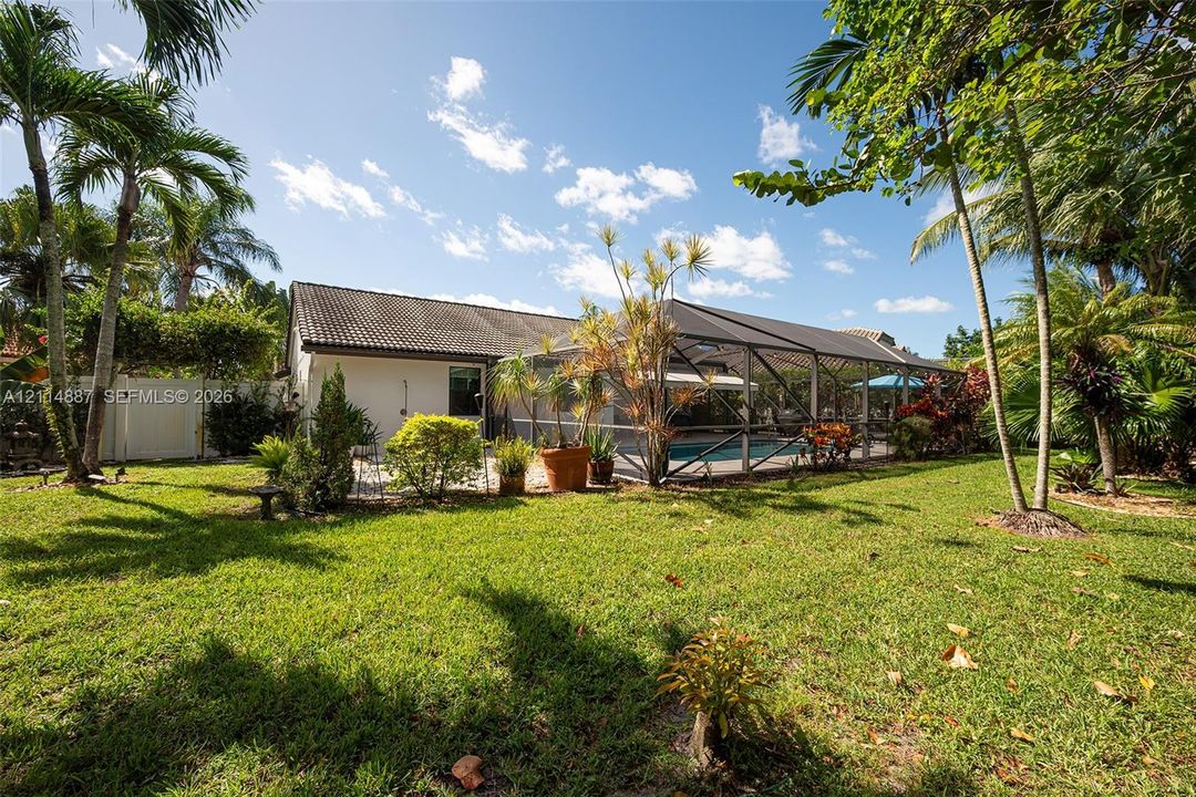 Spacious backyard featuring a manicured lawn, perimeter vinyl fencing, mature palm trees, and an enclosed screened-in pool area
