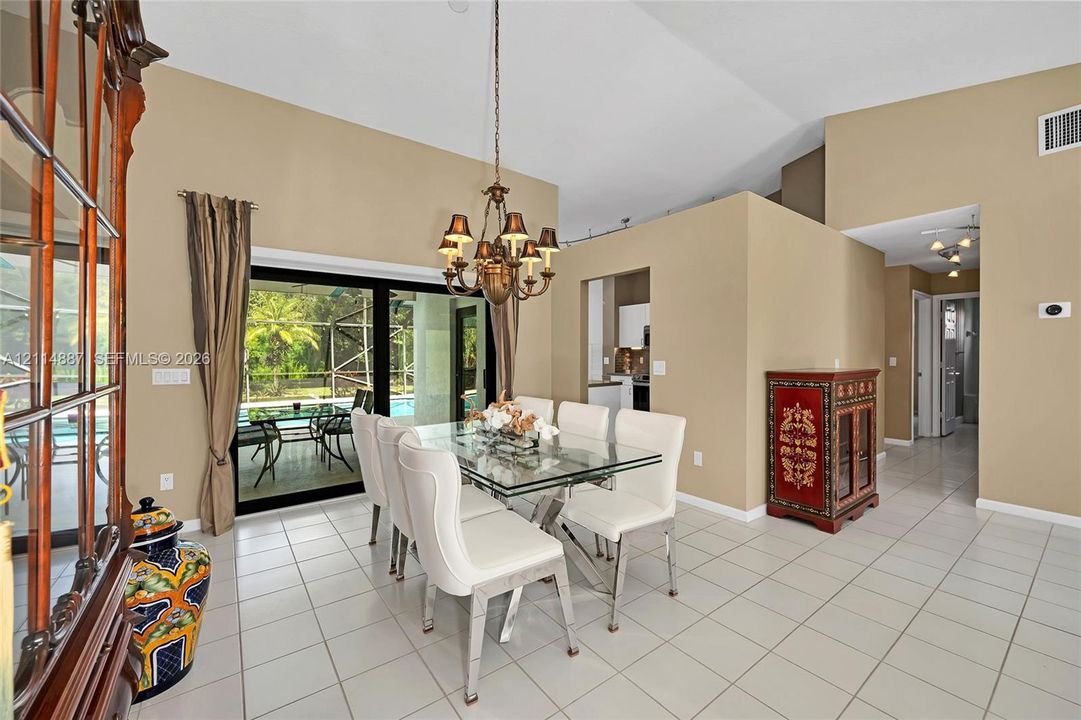 Dining area featuring vaulted ceilings, oversized ceramic tile flooring, a multi-arm chandelier, and sliding glass doors