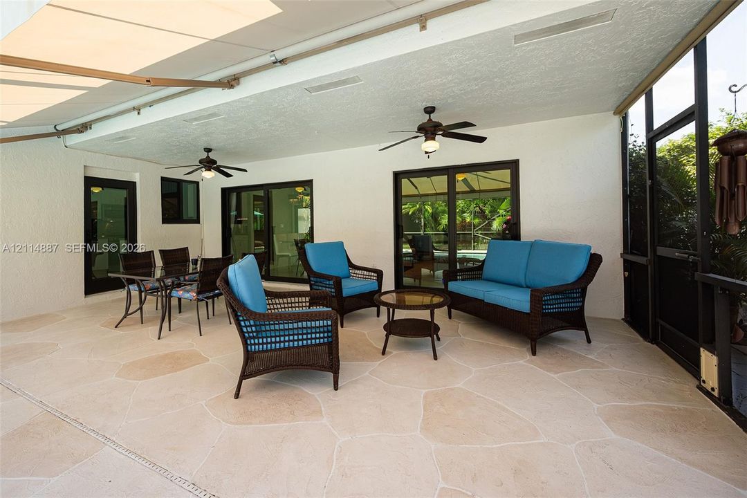 Covered patio featuring flagstone-style flooring, screen enclosure, dual ceiling fans, and sliding glass doors