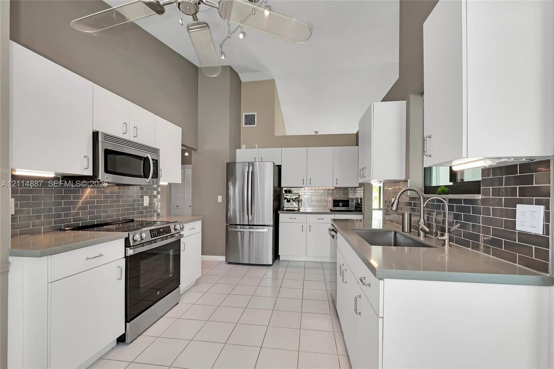 Kitchen featuring white cabinetry, grey subway tile backsplash, solid-surface countertops, stainless steel appliances, and tile flooring