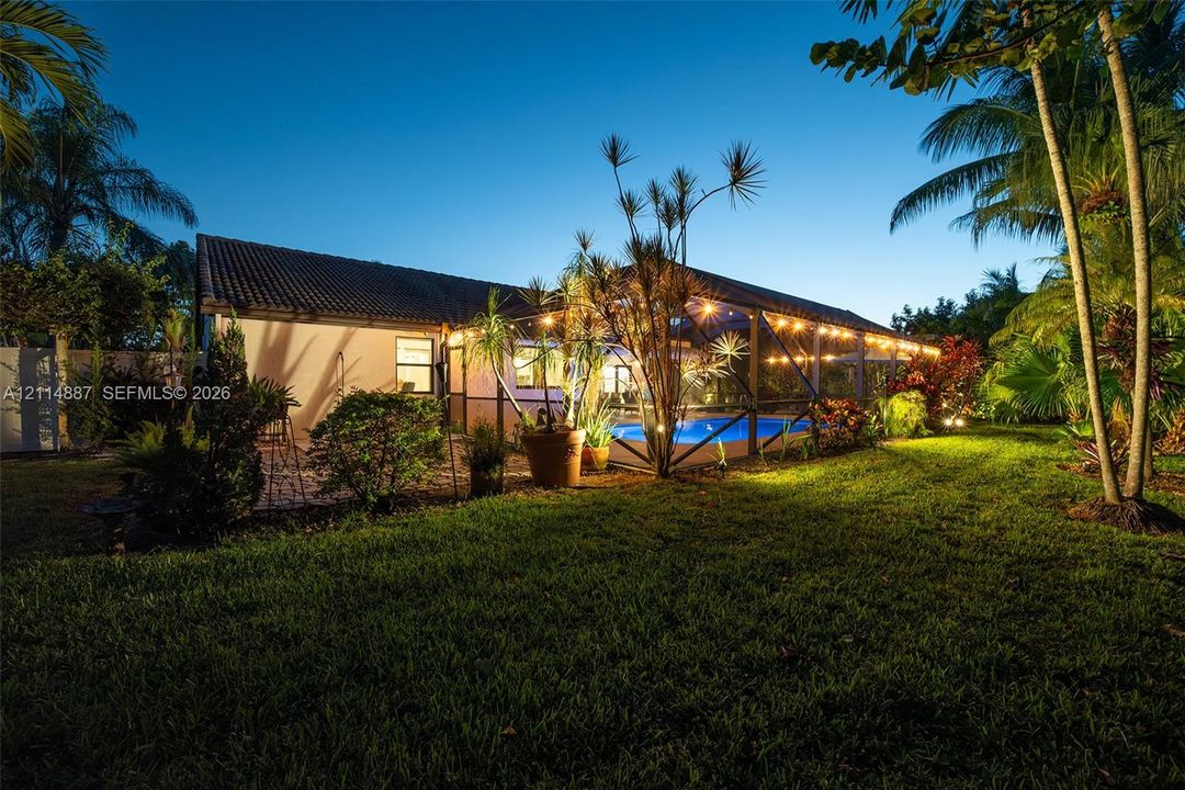 Backyard featuring a screened-in pool enclosure, paver patio, established landscaping, and palm trees