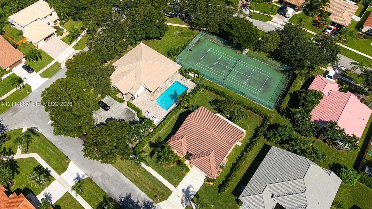 Aerial perspective featuring a private swimming pool, fenced-in tennis court, and lush landscaping